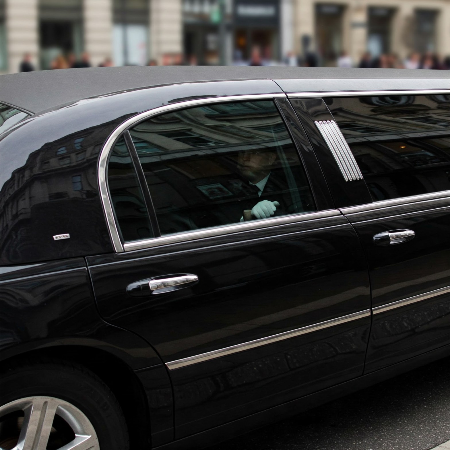A limousine with tinted windows in which one passenger is barely visible.